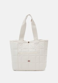 Kremowa pikowana torba na ramię z szerokimi tkaninowymi uchwytami, przednia kieszeń na zamek błyskawiczny oraz mała prostokątna łatka z logo umieszczona na środku poniżej zamka.