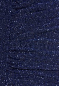 Marineblaue Stoff mit einer glänzenden, glitzernden Textur, die geraffte Bereiche aufweist und ein welliges Muster über die Oberfläche schafft.