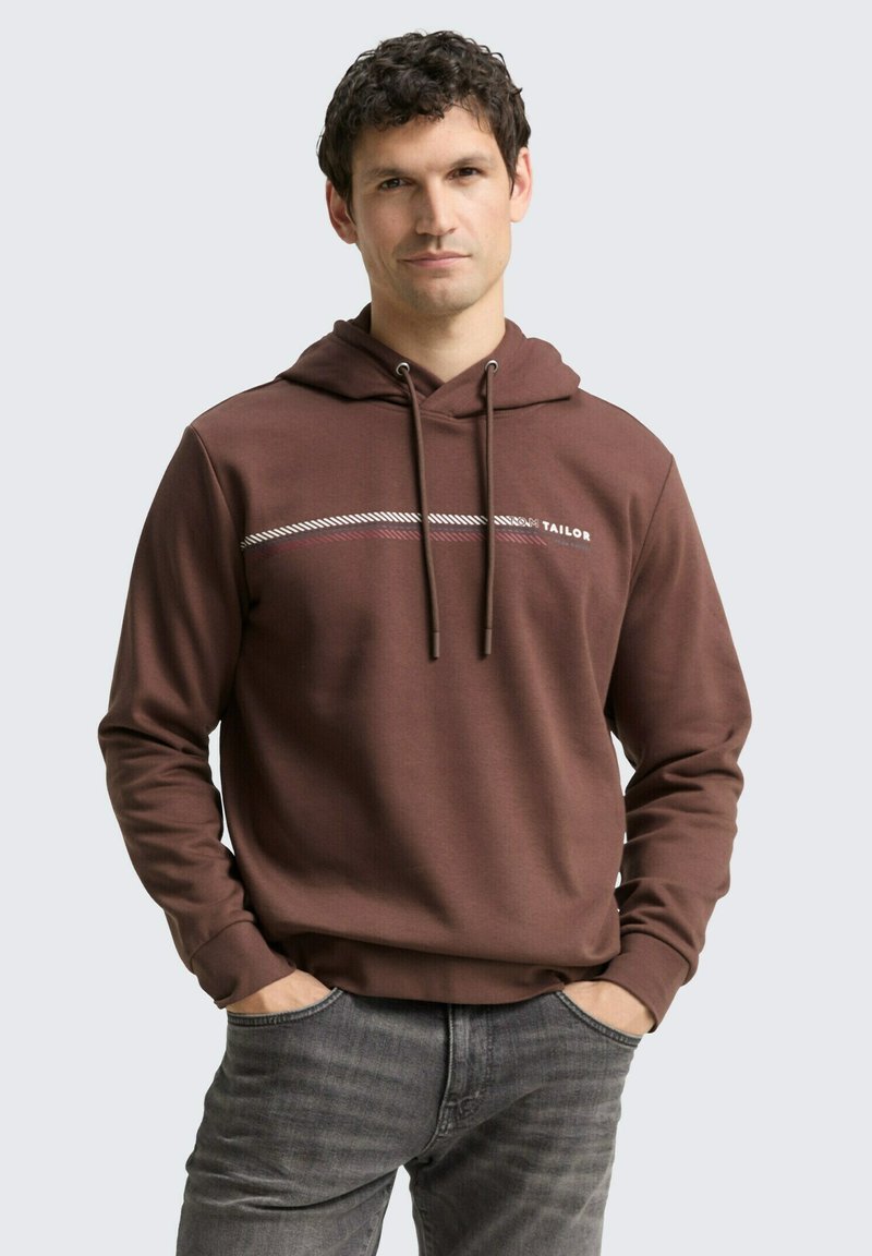 Bruine hoodie met trekkoorden, voorzien van witte en rode horizontale strepen over de borst. Soepele textuur, relaxte pasvorm en kangoeroezak.
