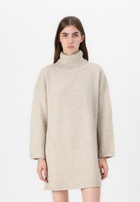 Beige strikket turtleneckkjole med oversized passform, lange ermer og en teksturert finish. Rett kantlinje som sitter over knærne.