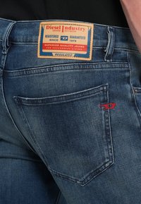 Blaue Jeans aus Denim mit einem Lederetikett der Marke "Diesel Industry". Sie verfügen über rote Nähte an der Tasche und eine ausgewaschene Textur.