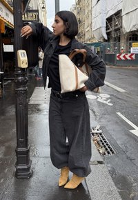 Svart denimjakke, svart T-skjorte og løse svarte jeans. Gule spisse ankelboots. Lys farget veske med brune håndtak. Fuktig gateomgivelse.
