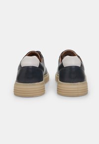 Navy leather sneakers with a white back panel, round shape, textured sole, and contrasting cream rubber outsole. Simple design with no visible detailing.