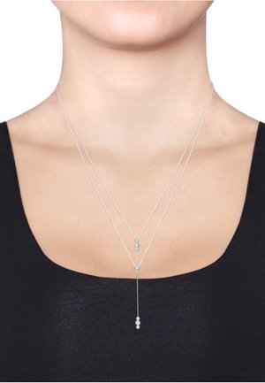 Zilveren driedelige ketting met cirkelvormige kristalaccenten, een centrale druppelhanger en fijne kettinglinks, gedragen op blote huid.