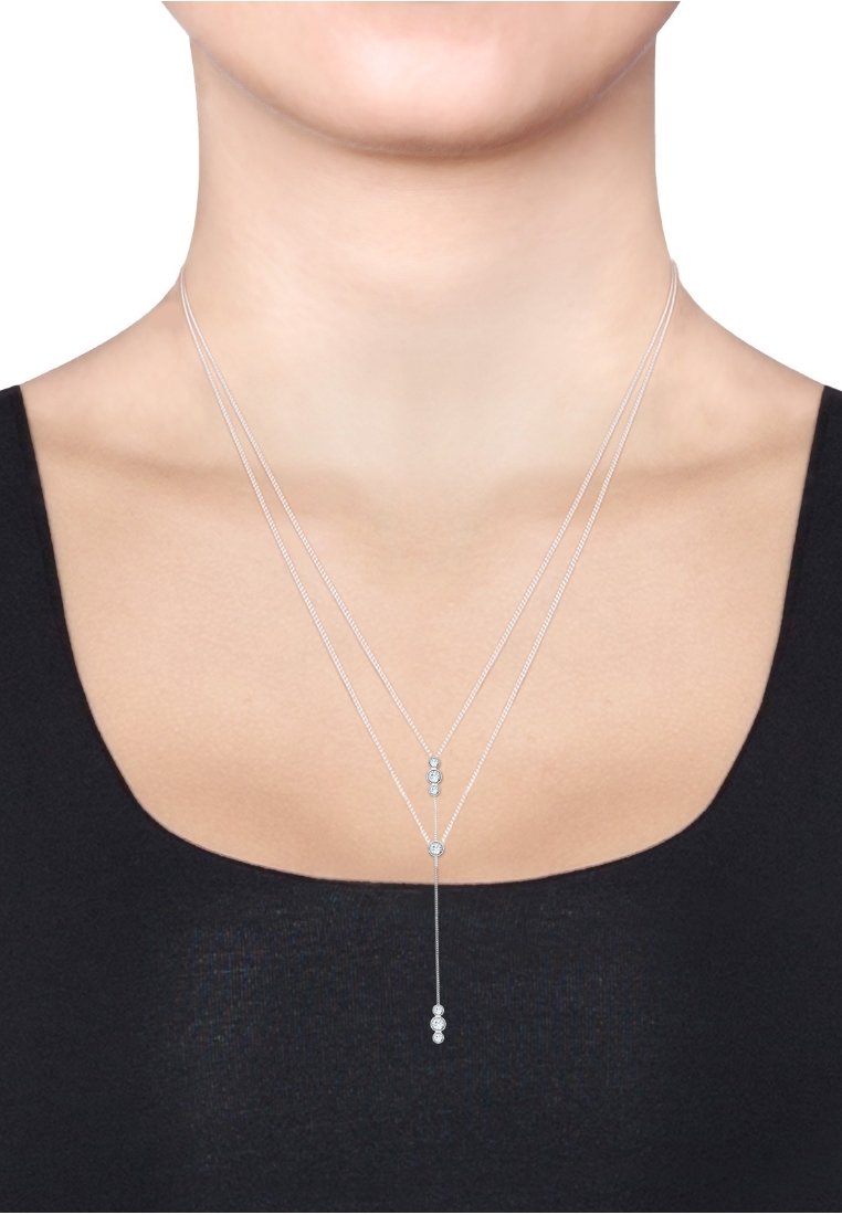 Zilveren driedelige ketting met cirkelvormige kristalaccenten, een centrale druppelhanger en fijne kettinglinks, gedragen op blote huid.