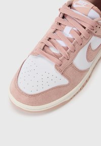 Sneaker Nike in suede rosa e pelle bianca. Punta rotonda con perforazioni, lacci piatti e suola imbottita.