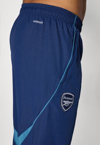 Marine atletik shorts med elastisk talje, med lyseblå detaljer og et broderet Arsenal-logo på den nederste side.