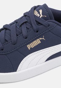 Tamno plave tenisice s bijelim naglascima i zlatnim Puma logotipom. Materijal: teksturirana sintetička gornjište. Karakteristike: okrugli vezice i gumeni potplat.