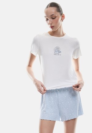 Camiseta blanca de manga corta con relieve y un gráfico bordado de luna y sol. Combinada con pantalones cortos de pijama azul claro que presentan un patrón de estrellas blancas.