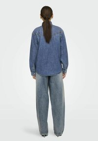Camicia di jeans e jeans a vestibilità ampia in blu medio. La camicia presenta un colletto classico e polsini con bottoni. Texture liscia con un design rilassato.