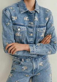 Chaqueta de denim y jeans a juego con bordados florales. Color azul claro, corte clásico, cierres de botón y bolsillos. Acentos florales en toda la prenda.