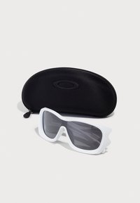 Óculos de sol brancos com um design ousado e angular e lentes graduadas, colocados ao lado de um estojo rígido oval preto com fecho de correr.