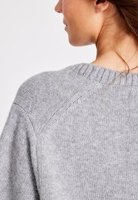 Helehall halli, millel on ribatud kaelus ja struktureeritud õlavarre seamid, esitatud seljapoolt, et rõhutada tekstuuri ja disaini.