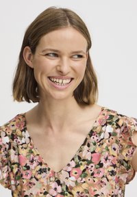 Blomstret kjole med V-udskæring, prydet med pink, hvide og grønne mønstre på en lys baggrund. Korte flæsekugler, blød stoftekstur.