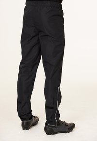 Zwarte waterdichte broek met een elastische tailleband, taps toelopend ontwerp, reflecterende accenten aan de zijkanten en klittenband sluitingen bij de enkels, gecombineerd met zwarte fietschoenen.