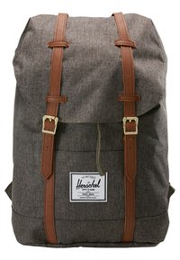 Sac à dos en tissu gris avec des sangles en cuir marron et des boucles dorées, doté d'une étiquette frontale avec le nom et le logo de la marque Herschel.
