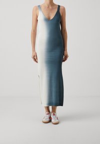 Robe longue à décolleté plongeant en V, présentant un dégradé ombré du blanc au bleu. Portée avec des baskets blanches à accents rouges et semelles en gomme.