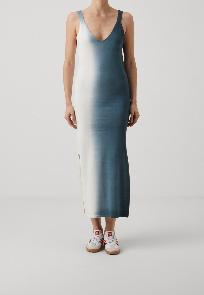 Robe longue à décolleté plongeant en V, présentant un dégradé ombré du blanc au bleu. Portée avec des baskets blanches à accents rouges et semelles en gomme.