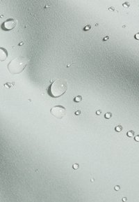 Des gouttelettes d'eau claires de tailles variées reposant sur un tissu lisse de couleur claire, mettant en valeur sa texture et sa surface déperlantes.