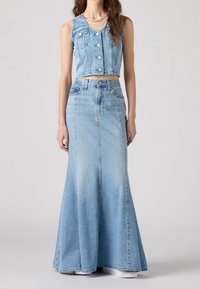 Conjunto de dos piezas de denim azul claro que consiste en un chaleco corto con botones y una larga falda maxi acampanada. Textura suave, diseño casual.