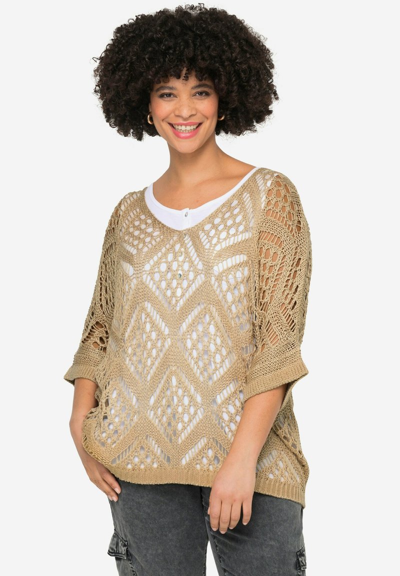 Licht beige gehaakte trui met een ruitpatroon en wijde mouwen, gedragen over een wit shirt. Getextureerde, losse pasvorm.