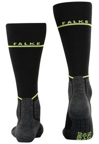 Knähöga svarta strumpor med gula accenter, med texturerade grå sulor och förstärkta häl- och tåområden. Varumärket "Falke" visas.