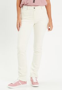 Jeans en denim blanc au design près du corps, avec cinq poches et une fermeture à boutons, associés à des baskets roses et une chemise rose pâle.