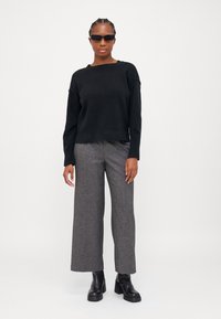 Sweater de malha preta com corte descontraído, combinado com calças largas cinzas e botins pretos de salto. Modelo usando óculos de sol ovais.