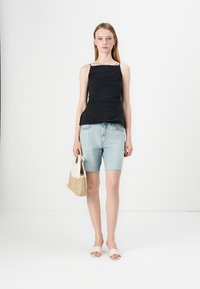 Zwarte, aansluitende, mouwloze top met verzamelde textuur; lichtblauwe denim shorts; witte slidersandalen; beige geknoopte handtas.