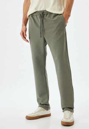 Grijze sweatpants met een elastische tailleband en verstelbaar trekkoord, gekenmerkt door een gestructureerde stof en rechte pijpen, in combinatie met witte sneakers.
