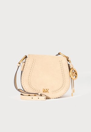Béžová kožená crossbody taška s pleteným lemom, zlatým logom MK a príveskom, nastaviteľným popruhom, na jednofarebnom svetlom pozadí.