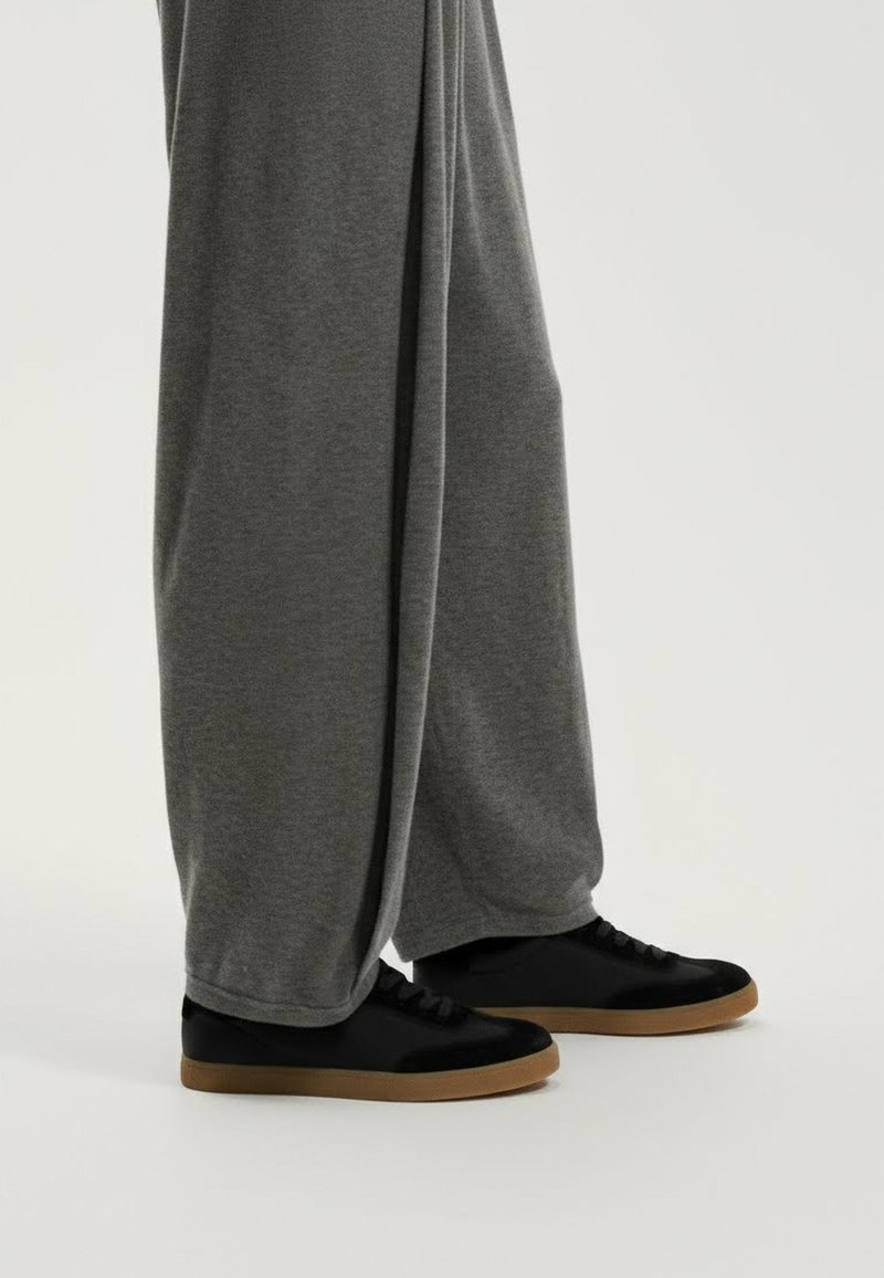 Pantaloni gri cu croială largă, realizați din țesătură moale, asortați cu adidași negri având partea superioară netedă și talpa texturată din cauciuc tăpăn.