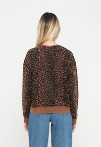 Sweater com estampa de leopardo castanho, de corte descontraído, com decote e punhos canelados, combinado com jeans de ganga azul clara. Textura de malha macia.