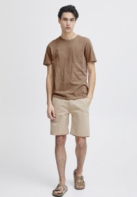 Hnědé tričko s krátkým rukávem a kapsou na prsou, světle béžové šortky a hnědé sandály na přezku. Jednoduchý, volnočasový letní outfit.