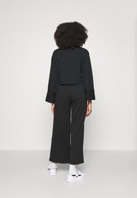 Top negro recortado de manga larga combinado con pantalones anchos negros, que ofrecen un ajuste relajado. Zapatillas blancas con detalles en negro completan el conjunto.