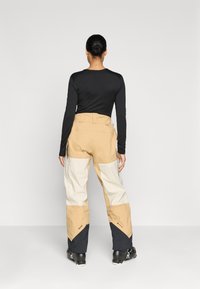 Skibroeken met een color-block ontwerp in beige, crème en zwart, met een losse pasvorm, gemaakt van duurzaam materiaal en met ritszakken aan de zijkant.