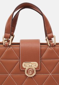 Borsa a tracolla in pelle marrone trapuntata con hardware dorato, chiusura con zip e cuciture a contrasto. Il manico è strutturato e resistente.