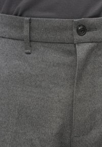 Szürke, texturált anyagból készült nadrág, gombos záródással, övbújtatókkal, testhezálló szabással és diszkrét halszálka mintával.