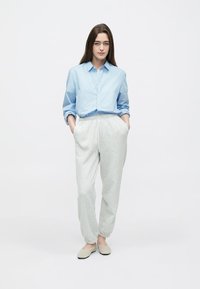 Svetlomodrá košeľa na gombíky s dlhými rukávmi, doplnená svetlosivými nohavicami so sťahovacou šnúrkou a béžovými nazúvacími topánkami. Jednoduchý, neformálny dizajn.