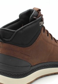 Zapato de cuero marrón con un cuello de textil negro. Presenta una puntera redondeada, diseño con cordones y una suela de goma negra texturizada.