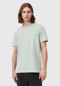 T-shirt verde chiaro a maniche corte realizzato in tessuto morbido, con scollatura rotonda e design semplice, abbinato a jeans scuri.