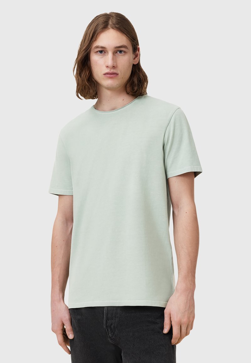 T-shirt verde chiaro a maniche corte realizzato in tessuto morbido, con scollatura rotonda e design semplice, abbinato a jeans scuri.