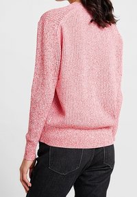 Maglione in maglia con texture di colore rosa chiaro, caratterizzato da un design a costine, maniche lunghe e scollatura rotonda. Indossato con jeans neri.