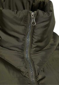 Detailní záběr na límec tmavě zelené péřové bundy s částečně zapnutým stříbrným kovovým zipem a hladkou texturou látky.