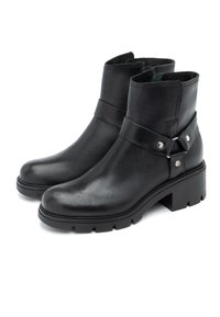 Mustat nilkkurit, jotka on valmistettu nahasta ja joissa on tekstuuri, varustettu hihnalla ja hopeanvärisillä yksityiskohdilla sivussa. Korkea, uritettu pohja.