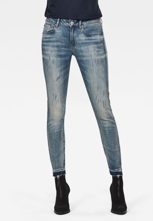 Jean bleu délavé à coupe slim avec des détails usés porté avec des bottines noires à fermeture éclair à l'avant.