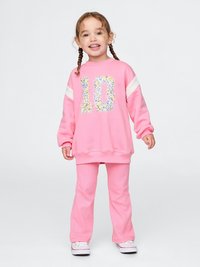 Pink sweatshirt with floral number 10 design, white shoulder stripes, paired with pink ribbed pants. Simple sneakers complete the outfit.