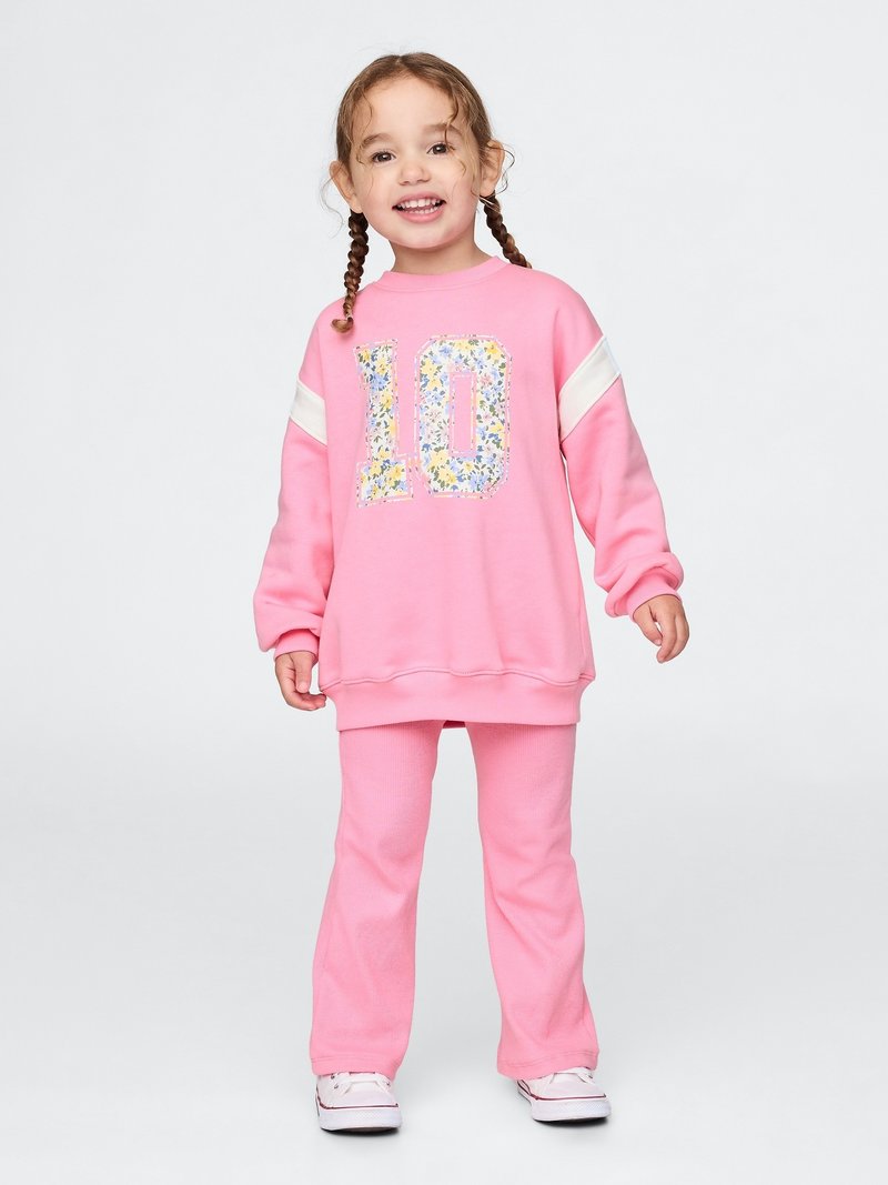 Pink sweatshirt with floral number 10 design, white shoulder stripes, paired with pink ribbed pants. Simple sneakers complete the outfit.
