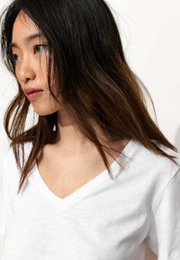 T-shirt en coton blanc avec un design en col en V. Texture douce, coupe décontractée, couture visible le long de l'encolure et manches légèrement amples.