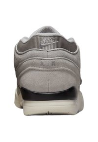 Tenis auriu din suede gri cu un superior din plasă texturată, având un accent pe călcâi negru și branding "AIR", precum și o talpă intermediară din cauciuc alb.